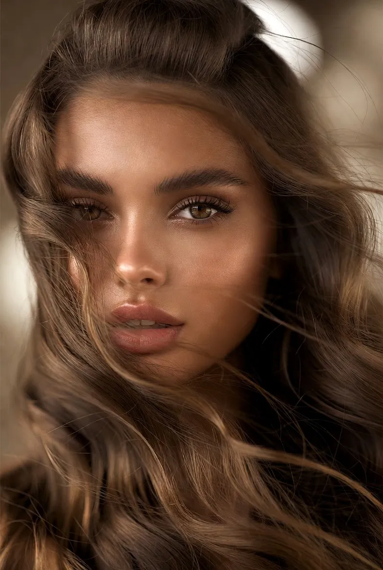 Ženska s svežo pomladno pričesko, valovitimi rjavimi lasmi in sijočo poltjo